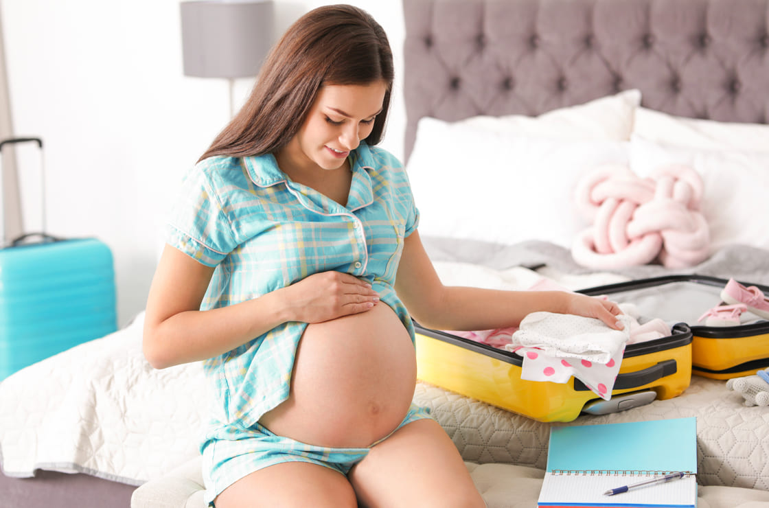 Futura mamá organizando la ropa del bebé dentro de la maleta de maternidad